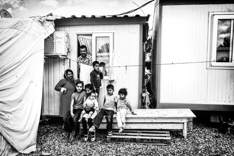 An Afghan family with six children stand outside their container on May 11, 2017 at Malakassa refugee camp in Greece. Photo illustration by Slate. Photo by Louisa Gouliamaki/AFP/Getty Images.